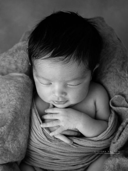 A black and white version of a newborn girl in a basket. The monochrome palette emphasizes the textures and her serene, sleeping form.