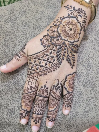 A close-up of a party henna design on the back of the hand, showing a beautiful floral cuff and intricate finger details.
