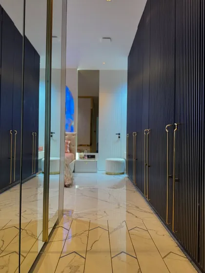 This walk-in closet, leading from the master bedroom, features deep blue fluted wardrobes with elegant gold handles. The full-length mirror at the end enhances the sense of space and reflects the beautiful bedroom beyond.