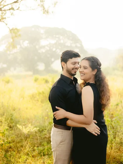 A happy, candid moment from an outdoor pre-wedding shoot. The couple is styled in classic black and neutral tones, creating a timeless look that allows their joyful interaction to be the main focus.