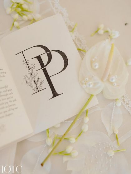 The personalized stationery for the home wedding, featuring the couple's initials and delicate floral illustrations, surrounded by fresh mogra and a pearl-studded anthurium.