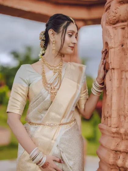 A close-up of the bride, focusing on her beautiful traditional gold jewellery and the soft fabric of her silk saree.