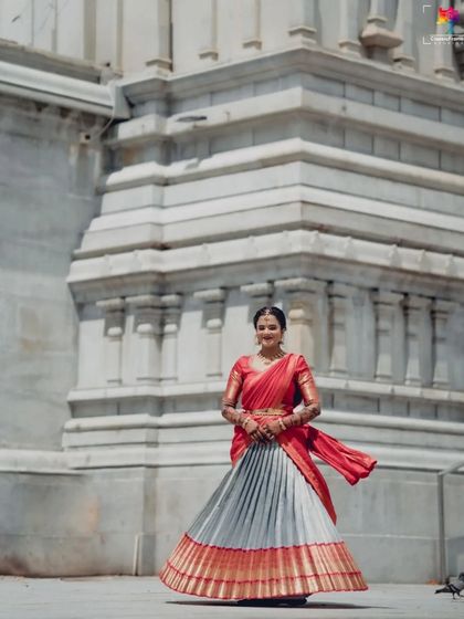A full-length portrait of the bride in her traditional half saree, standing before a magnificent temple. This shot captures the grandeur of both the attire and the location.