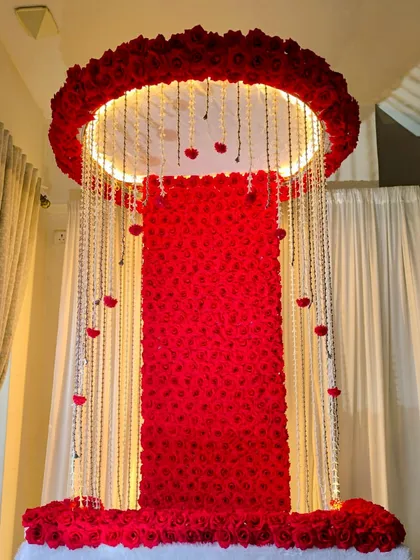 A grand Ganpati mandap made entirely of red roses. The circular top is illuminated and features hanging crystal strings, creating a dramatic and opulent look for the festival.