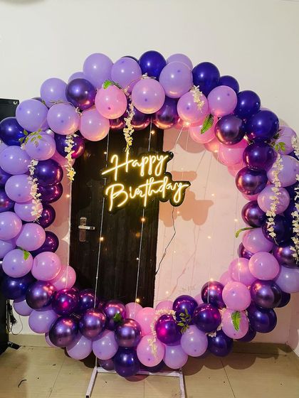 A beautiful full-ring balloon arch in shades of purple. This setup is perfect for creating a photo point in front of a door or plain wall, with a neon sign in the center.