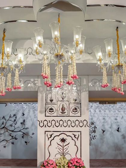 An elegant reception hall entrance featuring grand chandeliers adorned with jasmine and rose garlands. The walls are decorated with intricate mirror work and jaali patterns, creating a luxurious and traditional welcome.