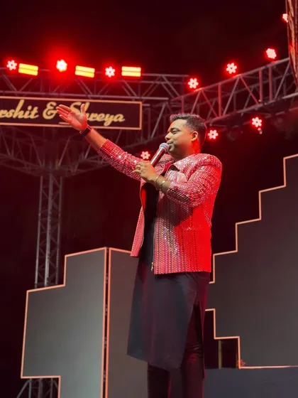 Addressing the audience during a sangeet night. The red stage lighting complements my sequined jacket, creating a visually stunning and energetic scene.