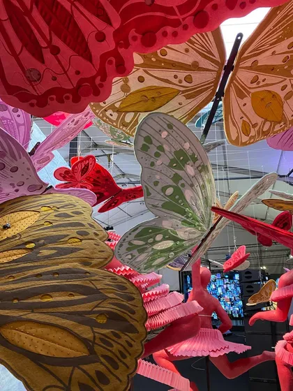 A close-up view looking up into the cloud of butterflies from the 'We/Us' installation. The layered paper wings create a rich tapestry of color and pattern.
