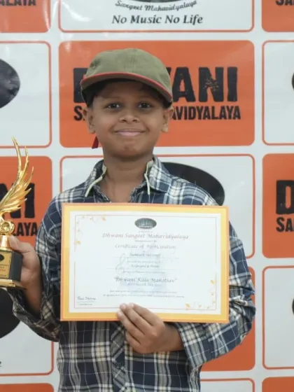 A young boy in a cap proudly holds his certificate and trophy.