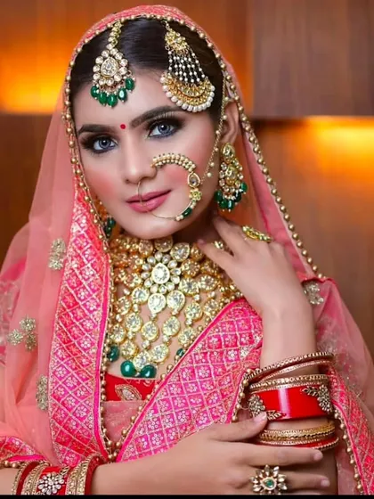A bride in a pink lehenga with a very heavy, royal Rajasthani bridal set. The jewellery features multiple layers, a large nath, and a statement borla.