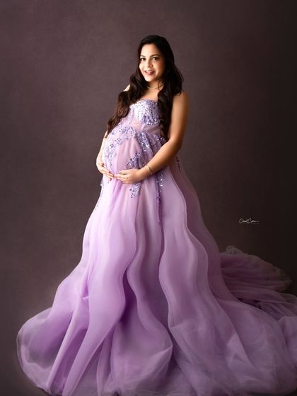 A classic, confident portrait. This mom-to-be cradles her bump in a beautiful lavender gown, radiating pure happiness.