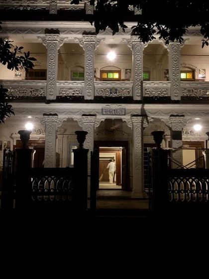 The inner courtyard of Rhodesia House at night, viewed from the entrance. The restored columns and balconies create a dramatic play of light and shadow, hinting at the layers of history contained within its walls and inviting exploration.