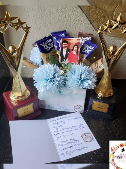 A gift combo featuring two custom trophies and a bouquet made of healthy Yoga Bars and flowers, celebrating 700 episodes of a show.