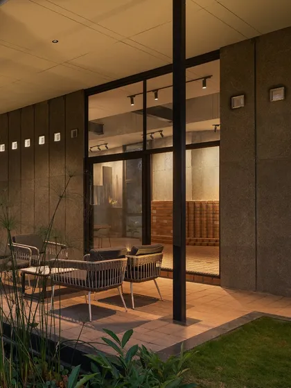 An outdoor seating area at 'The Earth', sheltered by the building's overhang. The large glass walls provide a seamless view into the warmly lit interior.