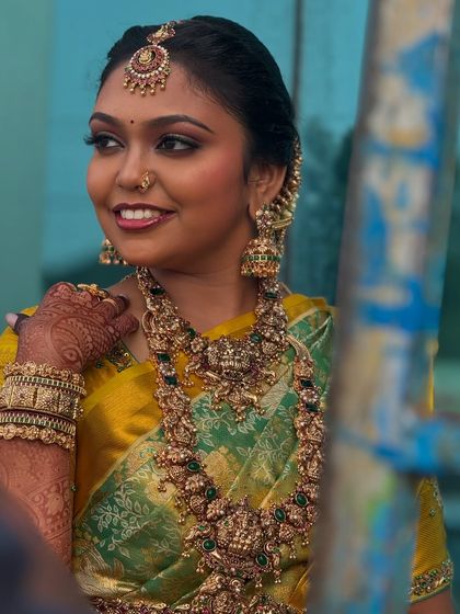 A candid outdoor shot of Prithivi. The natural light beautifully captures the details of her makeup and the richness of her antique gold jewellery.