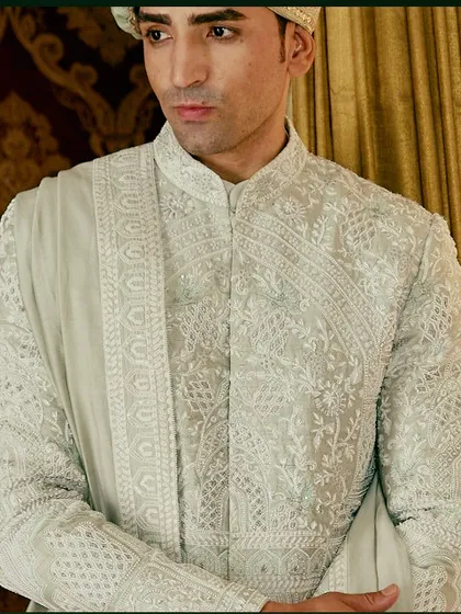 A close-up view of the intricate threadwork on the light green sherwani. The geometric and floral patterns are inspired by historical motifs, reimagined for the modern groom.
