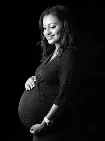 A beautiful black and white portrait with soft side lighting. The focus is on the mother's happy expression and the perfect curve of her belly.