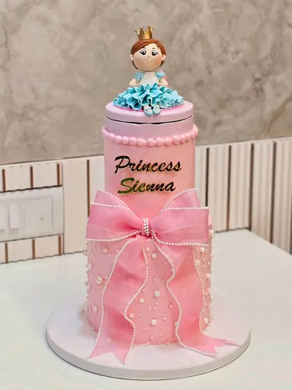 A tall, two-tier princess cake in pink, with a large bow and a princess figurine on top.