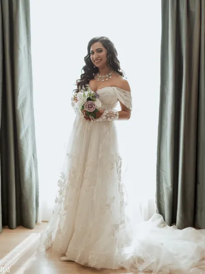 A beautiful bridal portrait, with the bride holding her bouquet and smiling, framed by soft window light.