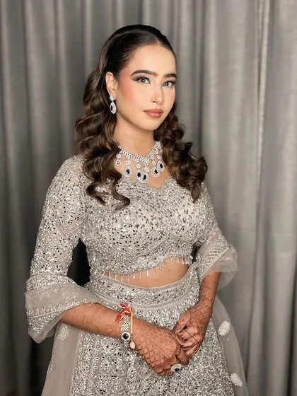Cocktail glam in a beautiful silver lehenga. The makeup features a subtle blue smokey eye to complement her jewelry, paired with soft, romantic curls.