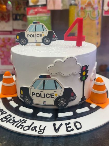 A fun police car theme cake for a 4th birthday. It features police car toppers, traffic cones, and a road design, making it an exciting cake for a child who dreams of being a police officer.
