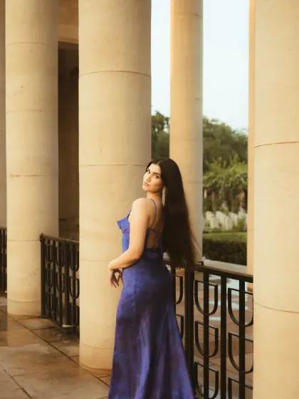 A wider shot from the same series, showing the wet ground and the grand pillars. The composition emphasizes the scale of the location and the elegance of the subject.