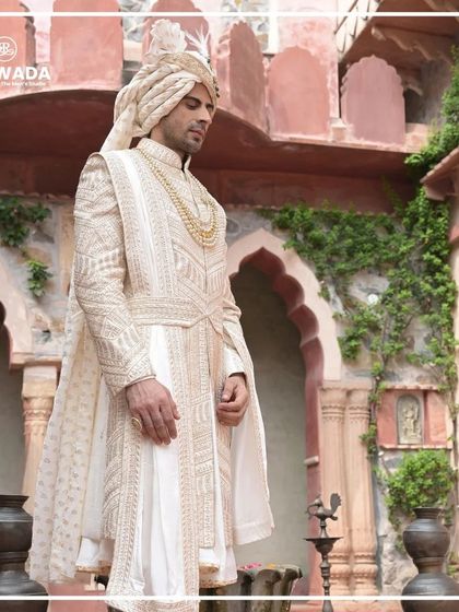 The groom looks away, creating a candid yet regal portrait. The flowing fabric of the sherwani and the intricate details are on full display.