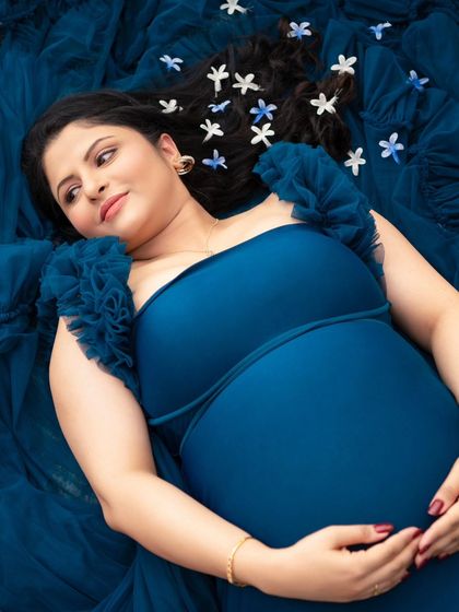 Lost in a dream. This overhead shot captures the mother-to-be lying on a bed of blue tulle, her expression peaceful and content. The small flowers scattered in her hair add a delicate, whimsical touch.