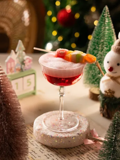 A whimsical Christmas cocktail garnished with candy. The festive props like the snowman and calendar set the scene perfectly.