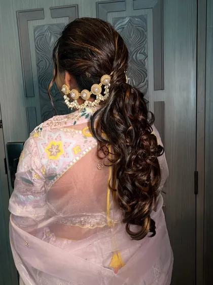 A chic and modern ponytail with soft curls and a statement pearl hair accessory. This hairstyle is perfect for a sangeet or reception look.