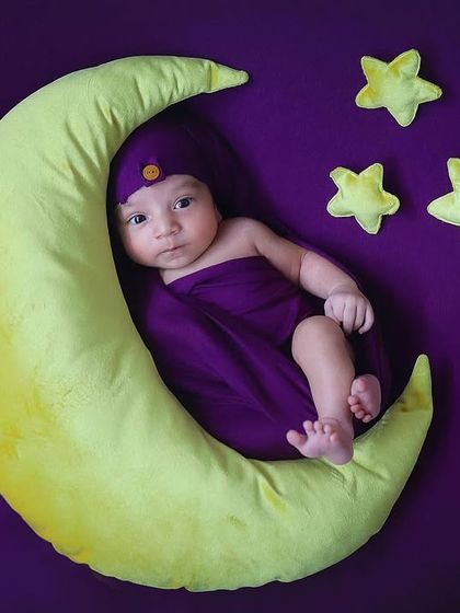 This little one is wide awake and looking curious. Posed on a crescent moon prop against a rich purple background, this is a fun and engaging take on the classic celestial theme.