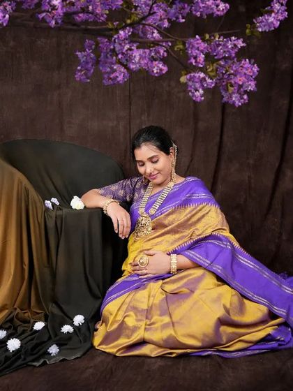 A serene portrait of a mother-to-be in a beautiful silk saree, seated by a blooming tree. The composition and colors create a peaceful and artistic image.