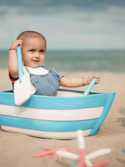 Ready to set sail. This little captain looks confident and cute as he holds his paddles in his toy boat on the beach.
