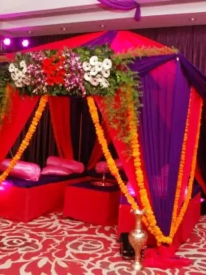 A cozy indoor tent canopy in purple and red, decorated with marigold garlands, creating a small, intimate space for a ceremony.