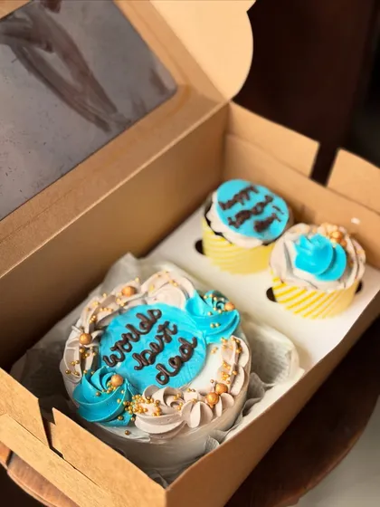 A close-up of the "World's Best Dad" bento and cupcake set, showcasing the detailed piping work in blue, white, and beige, with golden sprinkles for a festive touch.