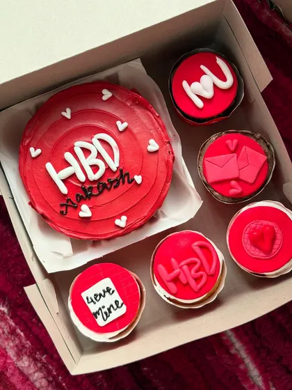 A bold red-themed birthday set for Akash. The bento cake is surrounded by six matching cupcakes with various designs like "love mine" and an envelope, making it a complete celebration package.