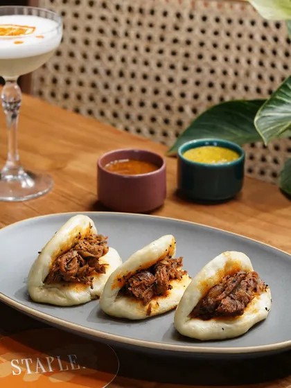 Showcasing these delicious pork bao buns with their accompanying dips. The composition is balanced with a refreshing cocktail to present a complete and satisfying meal option.