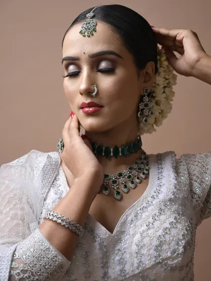 An elegant airbrush makeup look created as a demonstration for students, featuring a classic white saree with green jewelry. The skin finish is flawless.