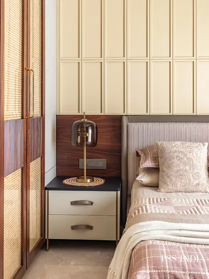 A close-up of the bedside table, featuring a modern lamp with a smoked glass shade that complements the warm wood and rattan wardrobe.