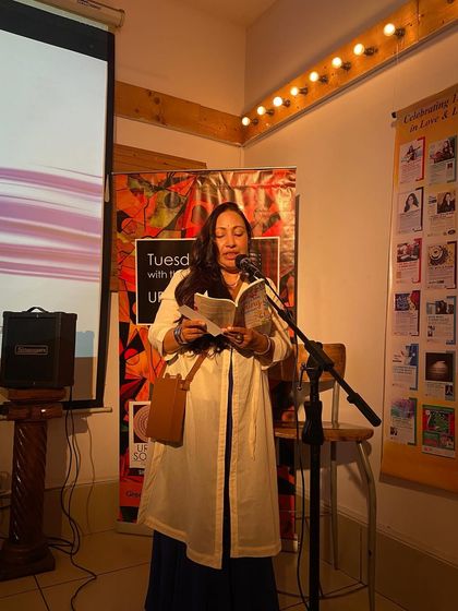 A poet stands at the microphone, reading from her book during our "An evening of Love poems" special. The warm lighting creates an intimate and focused mood.
