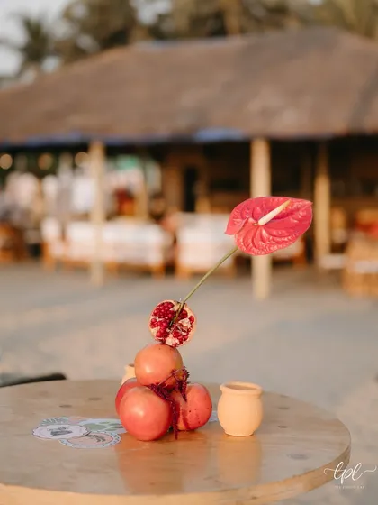 A small, artistic centerpiece of pomegranates and an anthurium on the beach.