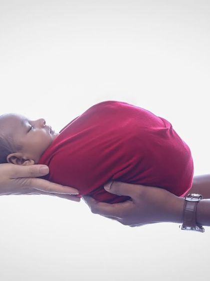 A beautifully simple and artistic photo of parents' hands supporting their swaddled newborn. This shot symbolizes the love and protection surrounding a new baby.