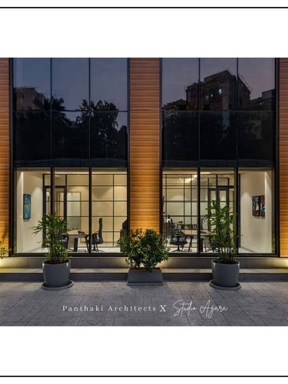 A close-up of the ground floor of the office building. The design uses a grid of large windows to create a sense of transparency and connection between the indoor workspace and the outside.