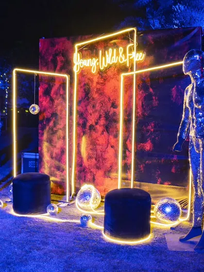 A 'Young, Wild & Free' neon sign creates a fun and energetic photo booth, flanked by shimmering metallic mannequins.