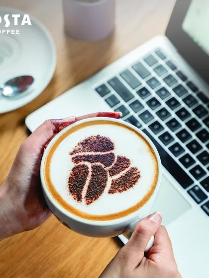 A perfect cup of coffee held over a laptop at Costa Coffee. It's the ideal companion for your workday, whether you're catching up on emails or preparing for your next big pitch.