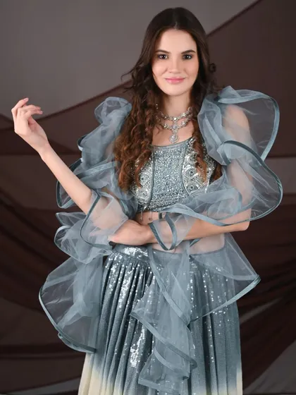 An international model showcases a unique grey and white ombre lehenga with dramatic ruffled sleeves. A great choice for a high-fashion shoot.