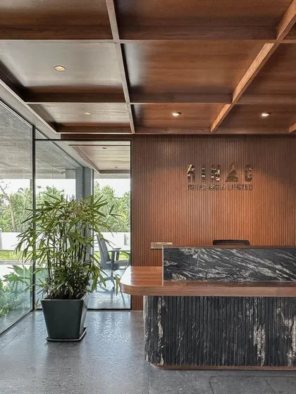 The reception area at RINAC Headquarters, designed to make a strong first impression. This space features a custom-designed desk with a fluted base and a dramatic black granite top, set against a backdrop of vertically grooved wood paneling and our signature coffered wood ceiling.