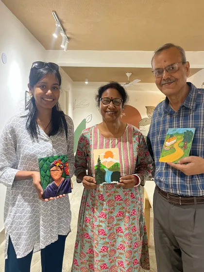 A family proudly displays their unique creations, including a Frida Kahlo portrait and a scenic landscape. Our studio encourages everyone to explore their own artistic interests.