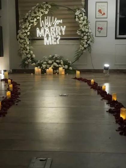 For a more intimate surprise proposal, I arranged this setup on a private terrace. It includes a circular ring backdrop adorned with white flowers, a 'Will You Marry Me?' neon sign, and a romantic path of candles and rose petals leading to the main display.