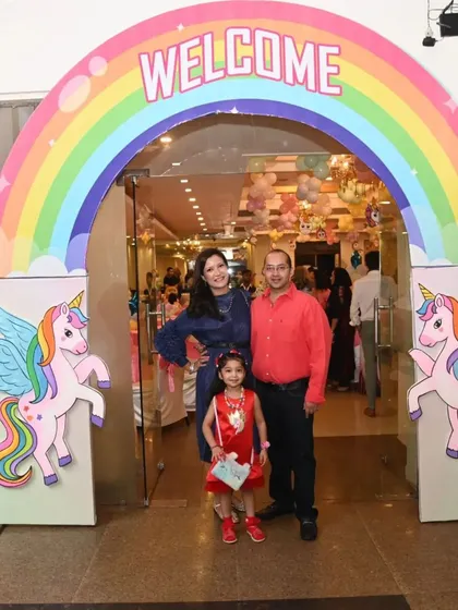 A magical rainbow entrance arch for a unicorn-themed party. The birthday girl and her family pose for a picture at this colorful and happy welcome gate.